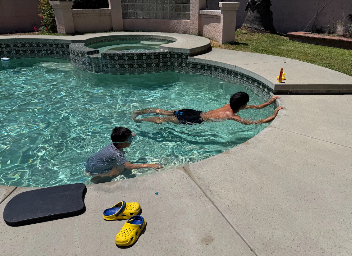 A young swimmer practicing a supported float while a coach swims alongside